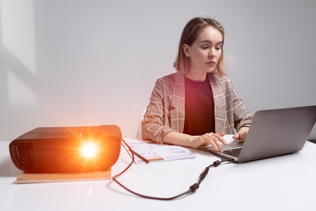 Piuttosto giovane imprenditrice seria o studente seduto a tavola davanti al computer portatile mentre si prepara per la presentazione per una conferenza o un seminario