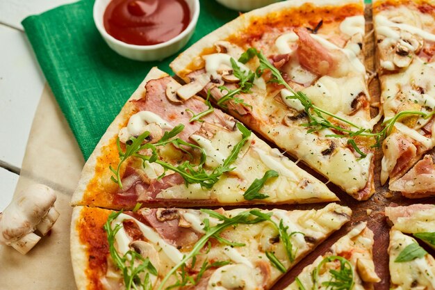 Pizza a fette appena sfornata con prosciutto rukkola e funghi serviti su sfondo di legno con salse di pomodoro ed erbe Concetto di consegna del cibo Menu del ristorante