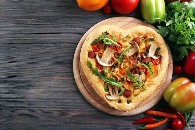 Pizza a forma di cuore e verdure fresche su fondo di legno