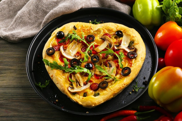 Pizza a forma di cuore su vassoio di metallo su fondo di legno