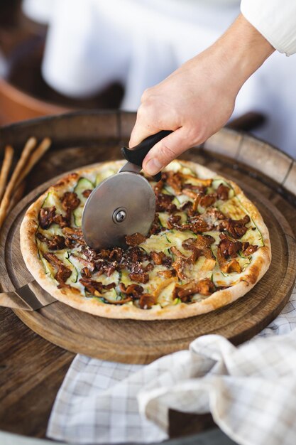 Pizza ai funghi su una tavola di legno. Servire la pizza. Lo chef taglia la pizza.