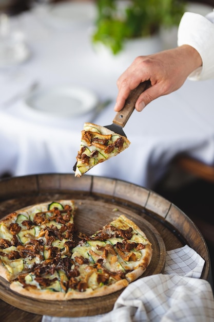 Pizza ai funghi su una tavola di legno. Servire la pizza. Lo chef taglia la pizza.