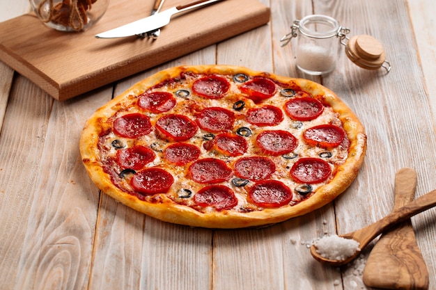 Pizza ai peperoni al forno fresco con salame e olive sul tavolo di legno