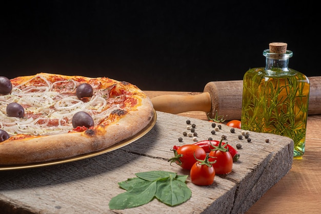 Pizza ai peperoni con cipolle, olive e origano su tavola di legno rustica