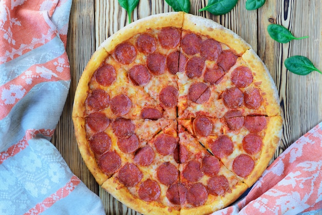 Pizza ai peperoni con spinaci e un asciugamano su una tavola di legno. Orientamento orizzontale, vista dall'alto.