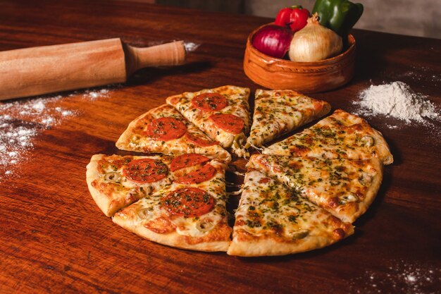 Pizza al formaggio e peperoni tagliata a pezzi su un tavolo di legno.