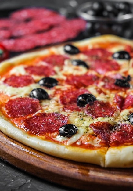 Pizza al salame con olive su una superficie scura