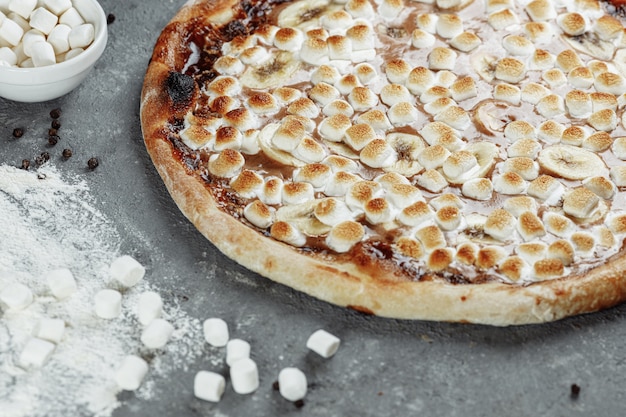 Pizza alla banana caramellata con crema di nocciole. Gli ingredienti sono pasta per pizza, banana a fette e crema di nocciole.