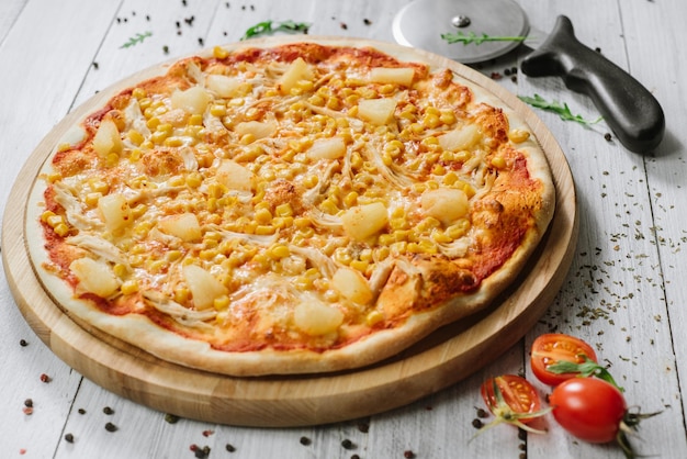 Pizza americana con mozzarella, filetto di pollo, ananas e mais sullo sfondo di legno