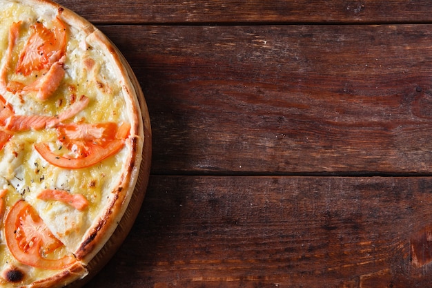 Pizza appetitosa al forno con formaggio, pomodoro e salmone, piatta. Fast food italiano servito su tavola rustica in legno, spazio libero per il testo.