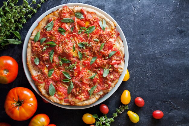 Pizza appetitosa con pomodori su una superficie scura