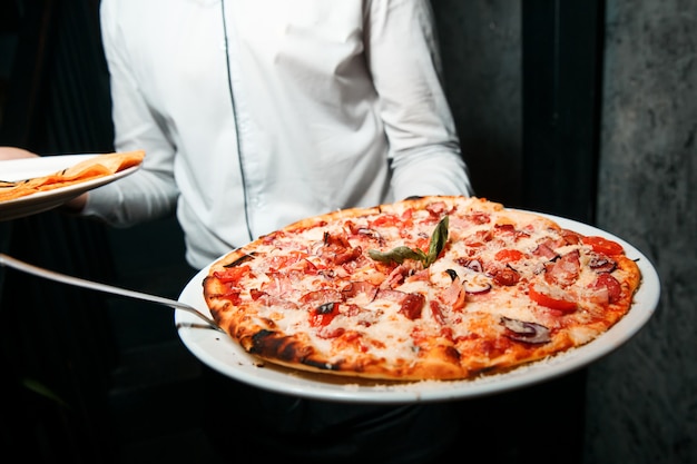 Pizza calda con formaggio fuso, pomodori e prosciutto. Servito su un piatto bianco e rotondo. Croccante.