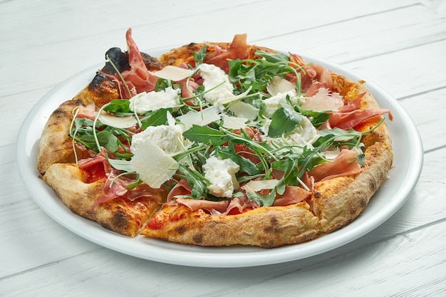 Pizza casalinga appetitosa con jamon, parmigiano, rucola e straccella su un piatto bianco su un bianco