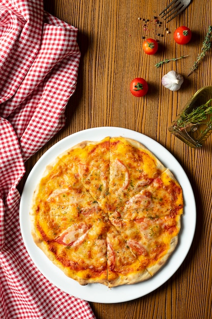 Pizza casalinga fresca della margarita su un fondo di legno in composizione con un panno rosso e un olio d'oliva. Cucina italiana. Foto di cibo vista dall'alto