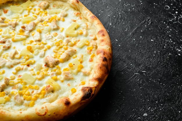 Pizza classica con pollo, ananas e formaggio Pizza al formaggio su sfondo di pietra nera Vista dall'alto