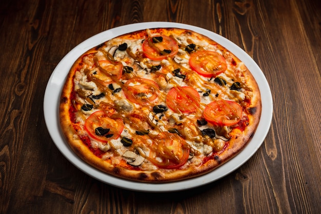 Pizza con carne di pollo, funghi, pomodori e olive nere, fondo in legno, scuro