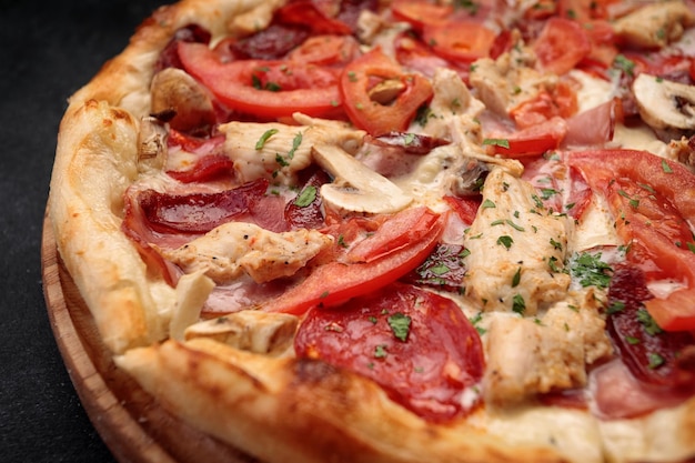 Pizza con carne di salsiccia di funghi di pollo e pomodori Su una tavola di legno su uno sfondo scuro