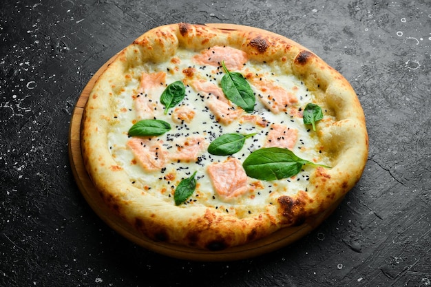 Pizza con formaggio di salmone e spinaci pizza classica su uno sfondo di pietra nera vista dall'alto