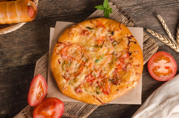 Pizza con formaggio e pomodori su un primo piano del fondo di legno con gli ingredienti