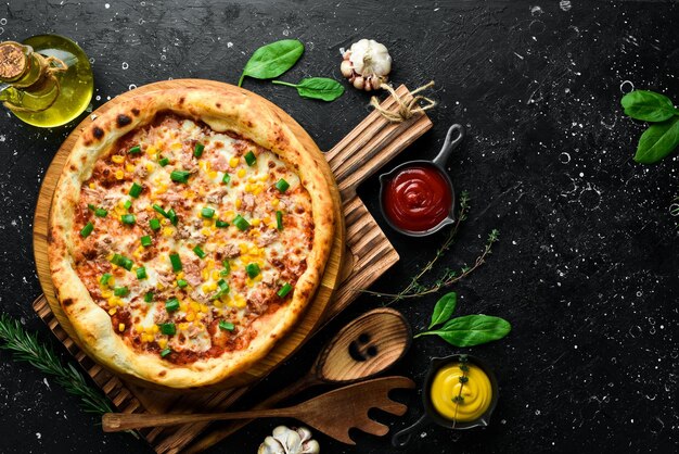 Pizza con mais di tonno e formaggio pizza classica su uno sfondo di pietra nera vista dall'alto