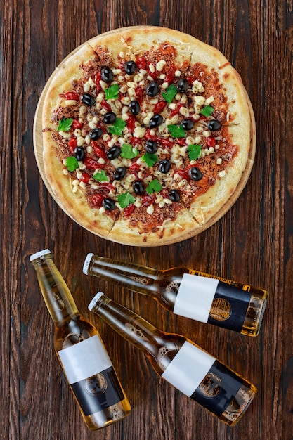 Pizza con olive, mozzarella e verdure e tre bottiglie di birra su un fondo di legno. Visualizza dall'alto. Immagine pubblicitaria, banner