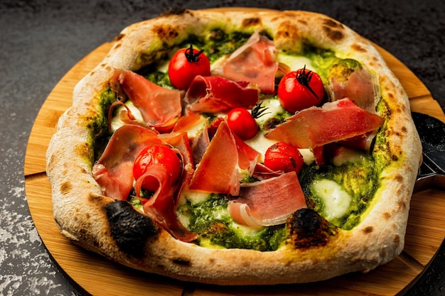 Pizza con pesto di pomodorini di carne di prosciutto e formaggio servito su un primo piano di tavola di legno