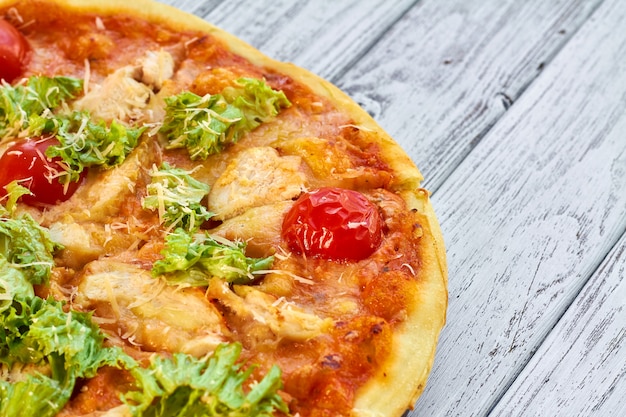 Pizza con pollo, pomodori e formaggio sul tavolo di legno