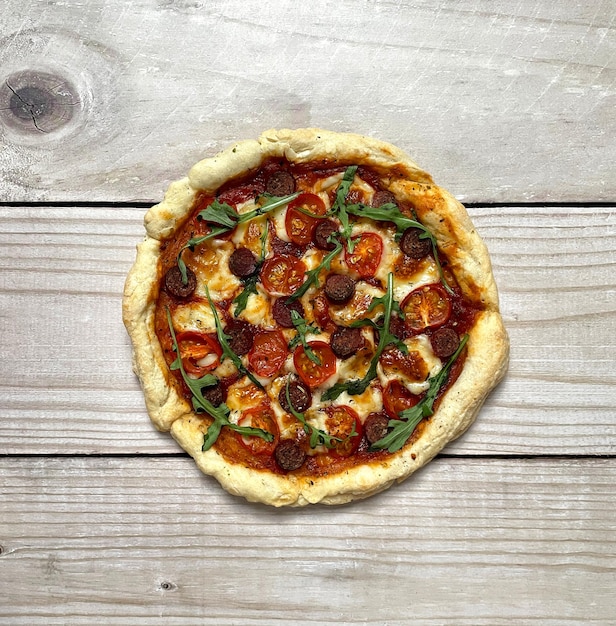 Pizza con pomodori, salsicce, parmigiano ed erbe aromatiche isolate su sfondo di legno. Vista dall'alto.