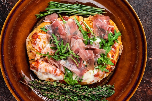 Pizza con prosciutto di Parma, insalata di rucola e parmigiano in un piatto rustico. fondo in legno. Vista dall'alto.