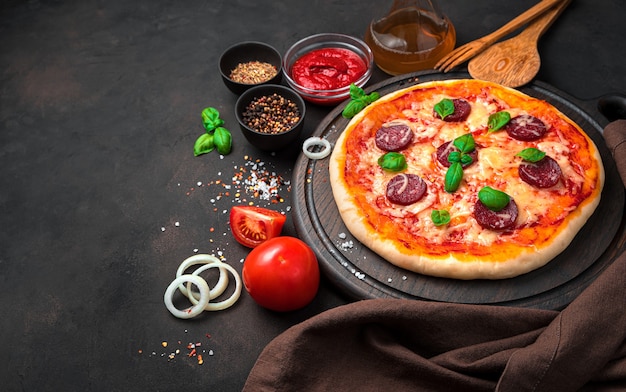 Pizza con salame, formaggio e pomodori su uno sfondo di cemento marrone.