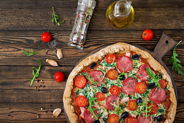 Pizza con salame, pomodori, olive e formaggio su un impasto con farina integrale. Cibo italiano. Vista dall'alto. Disteso.