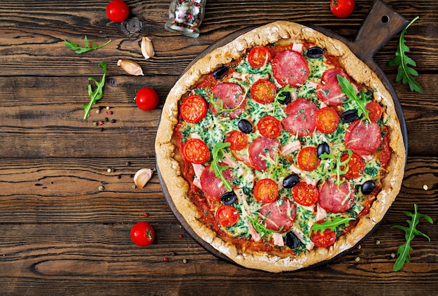 Pizza con salame, pomodori, olive e formaggio su un impasto con farina integrale. Top vie