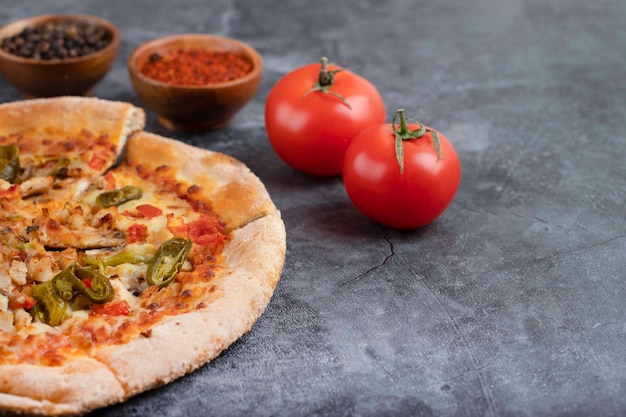 Pizza deliziosa calda affettata con pomodori rossi freschi posti su un tavolo di pietra.