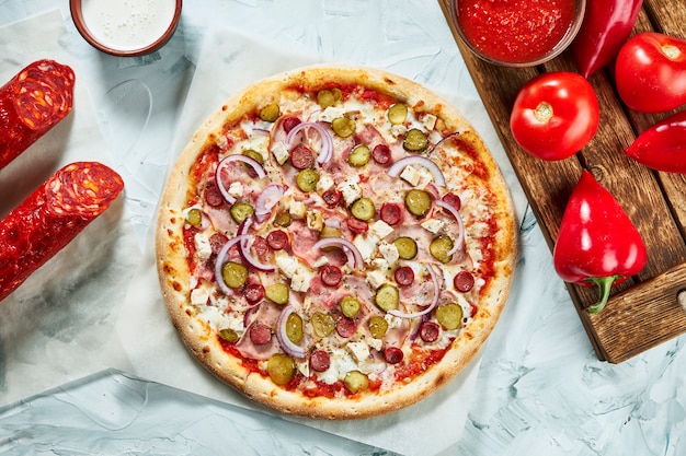 Pizza di carne al forno fatta in casa con cipolle, formaggio, prosciutto, cetrioli sottaceto con salsa rossa. Composizione con pizza croccante, pomodori.