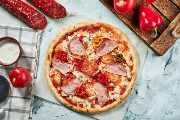 Pizza di carne al forno fatta in casa con pomodori, formaggio, prosciutto, salsa rossa. Composizione con pizza croccante, pomodori .. Vista dall'alto