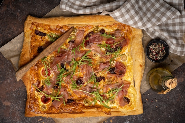 Pizza di pasta sfoglia con affettati, rucola, olive, spezie