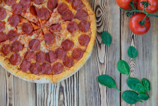 Pizza di peperoni con spinaci e pomodori su una tavola di legno. Orientamento orizzontale, vista dall'alto.