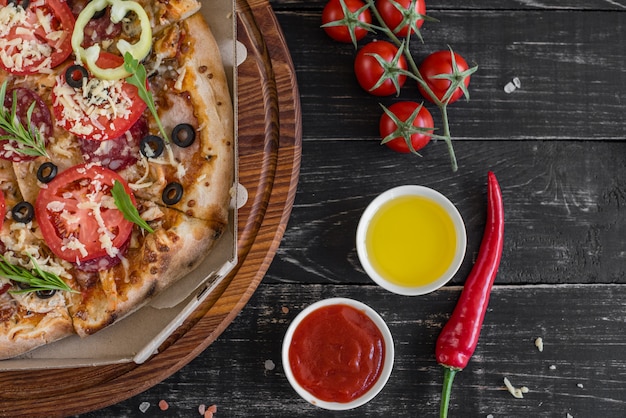 Pizza di verdure, funghi e pomodori su un fondo di legno nero. Può essere usato come sfondo