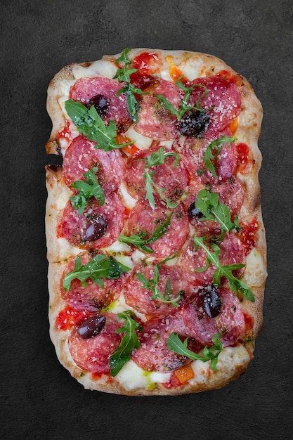 Pizza Diavolo con chorizo rucola jalapeno peperoncino kalamata pesto Pizza romana rettangolare su sfondo scuro