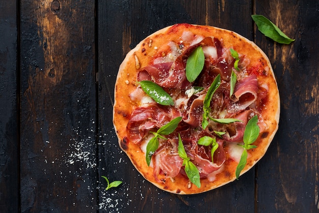 Pizza fatta in casa con jamon, mozzarella e foglie di basilico su un vecchio fondo di legno. Vista dall'alto.