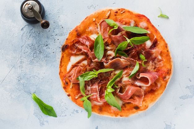 Pizza fatta in casa con jamon, mozzarella e foglie di basilico su vecchio fondo concreto. Vista dall'alto.