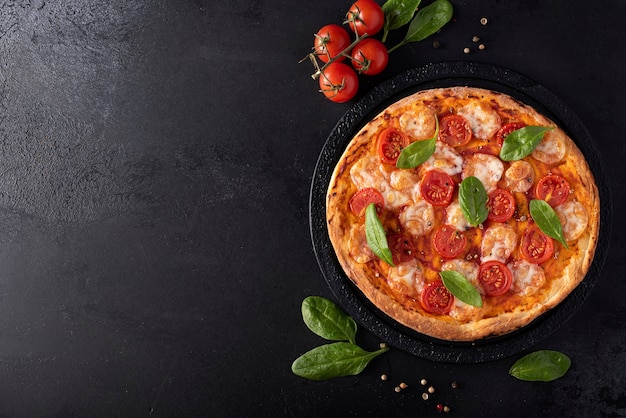 Pizza fatta in casa con mozzarella e pomodorini su una tavola rotonda nera, vista dall'alto