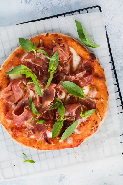 Pizza fatta in casa con prosciutto, mozzarella e foglie di basilico fresco