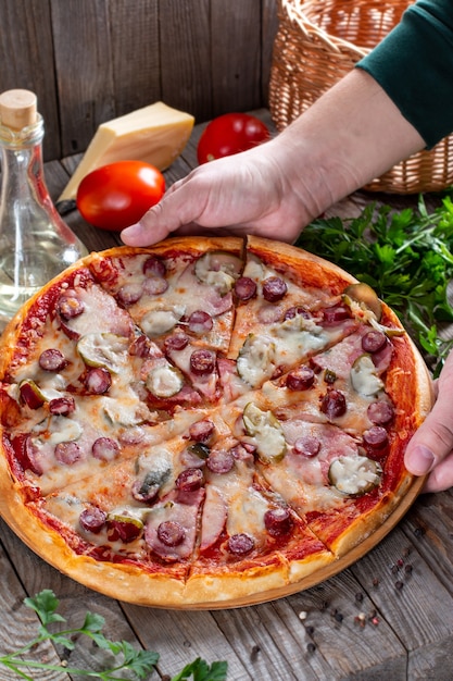 Pizza fatta in casa con salsiccia, sottaceti, pomodoro e formaggio su un tavolo. Cibo gustoso