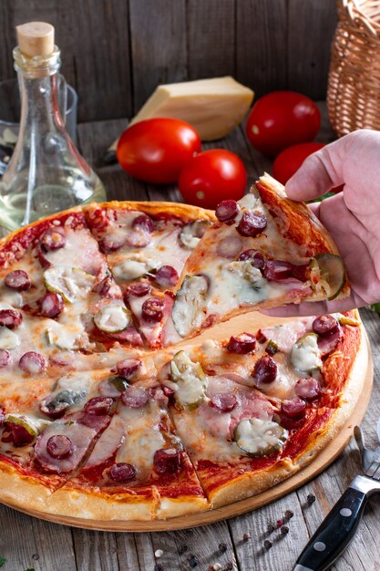 Pizza fatta in casa con salsiccia, sottaceti, pomodoro e formaggio su un tavolo. Cibo gustoso
