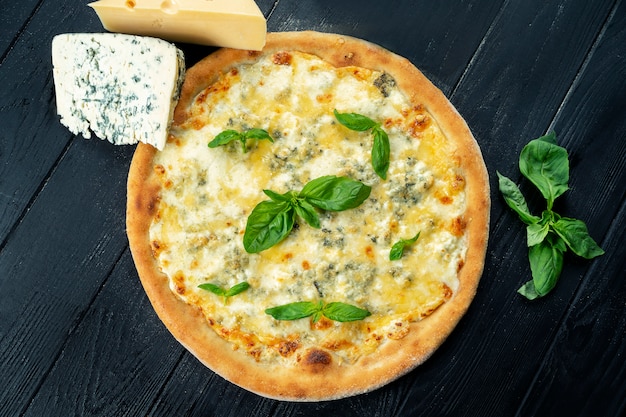 Pizza fresca fatta in casa con quattro formaggi e basilico su un legno nero con spazio di copia. Foto di cibo vista dall'alto. Disteso. Cucina italiana.