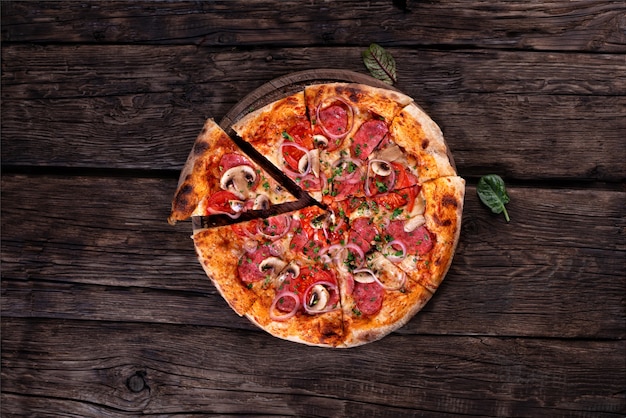 Pizza intera con salame e funghi piatta adagiata su uno sfondo scuro in stile rustico. Fast food. Cibo sano, concetto di alimentazione biologica e naturale. Cibo italiano.