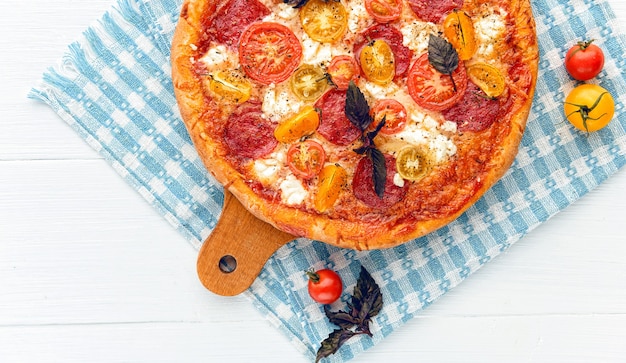 Pizza italiana ai peperoni con salame e formaggio su fondo bianco in legno rustico