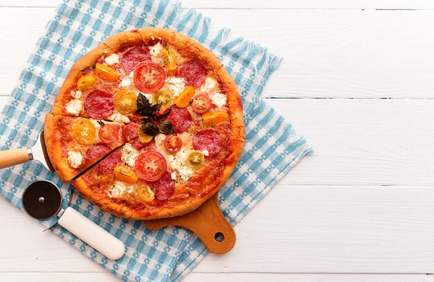 Pizza italiana ai peperoni con salame e formaggio su fondo bianco in legno rustico