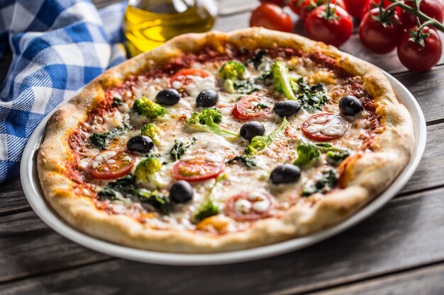 Pizza italiana con broccoli spinaci pomodori olive e mozzarella o parmigiano. Pasto vegetariano mediterraneo.